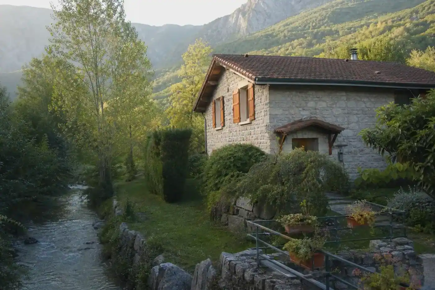 maison traditionnelle en pierre apparente proche d'une rivière, volets bois colorés, jardin arboré, lumière de fin de journée, aucune personne visible