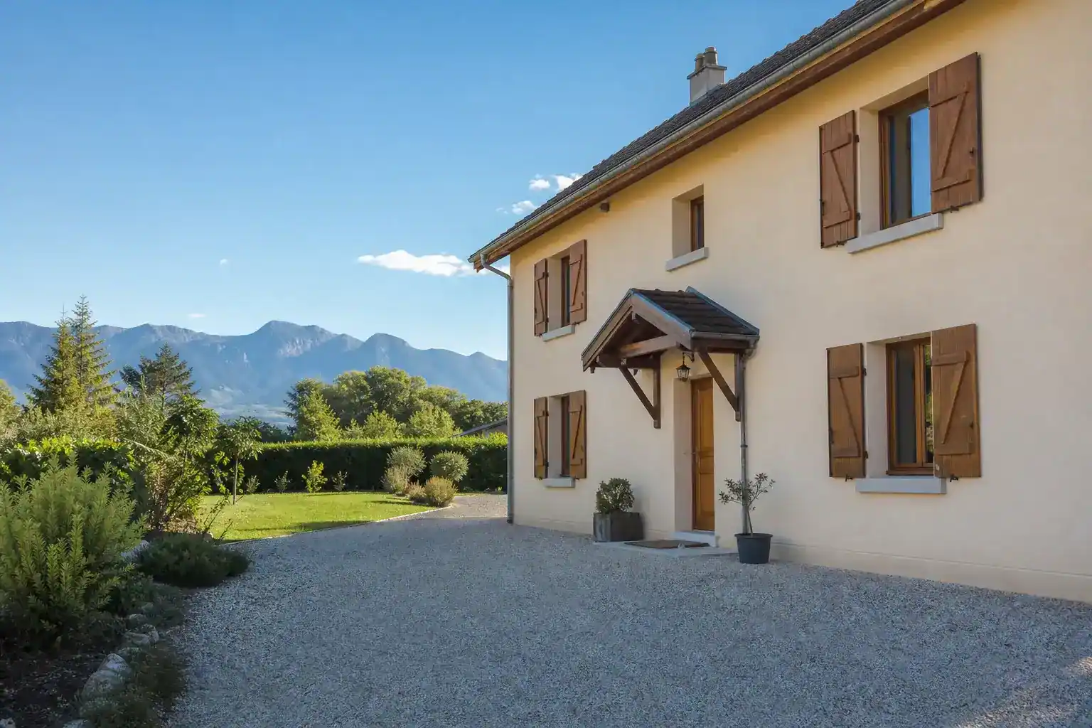 maison traditionnelle à étage, façade enduite ton pierre claire, allée gravillonnée, cadre rural en arrière-plan, journée ensoleillée, aucune personne visible