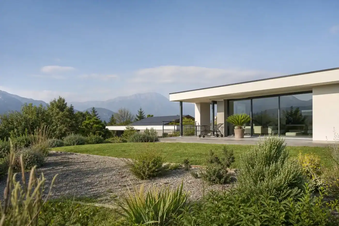 maison contemporaine à toit plat avec grande baie vitrée sur jardin, végétation méditerranéenne discrète, lumière de fin de matinée, aucune personne visible