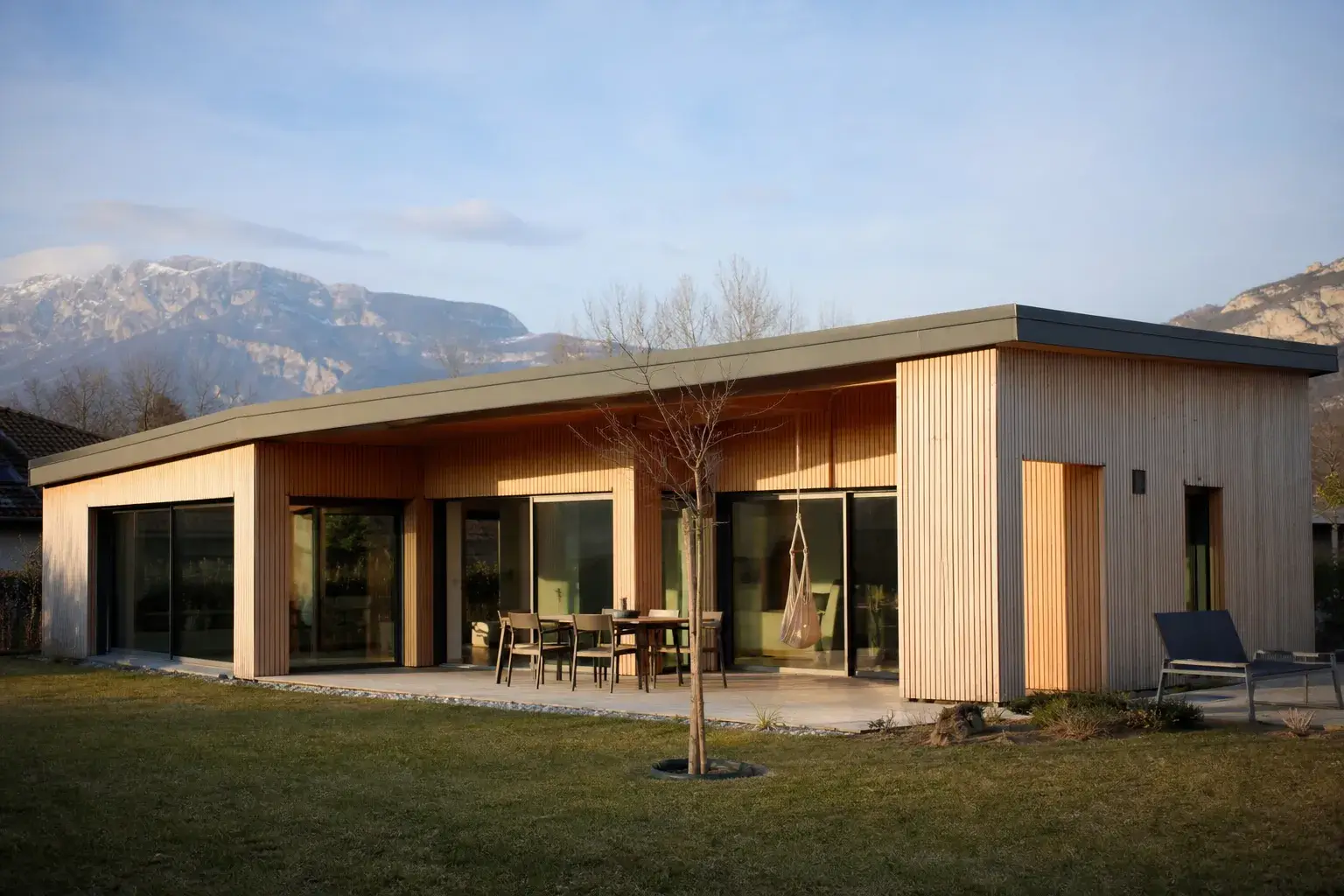 hero service ossature bois : maison contemporaine bardage bois clair, toit a faible pente, jardin engazonné, lumière fin d'après-midi, aucune personne visible