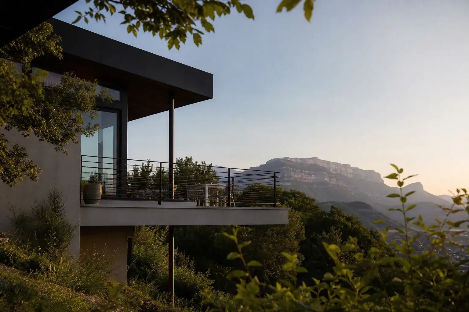maison contemporaine à flanc de coteau avec terrasse en surplomb, vue dégagée sur relief montagneux en arrière-plan, fin de journée, aucune personne visible