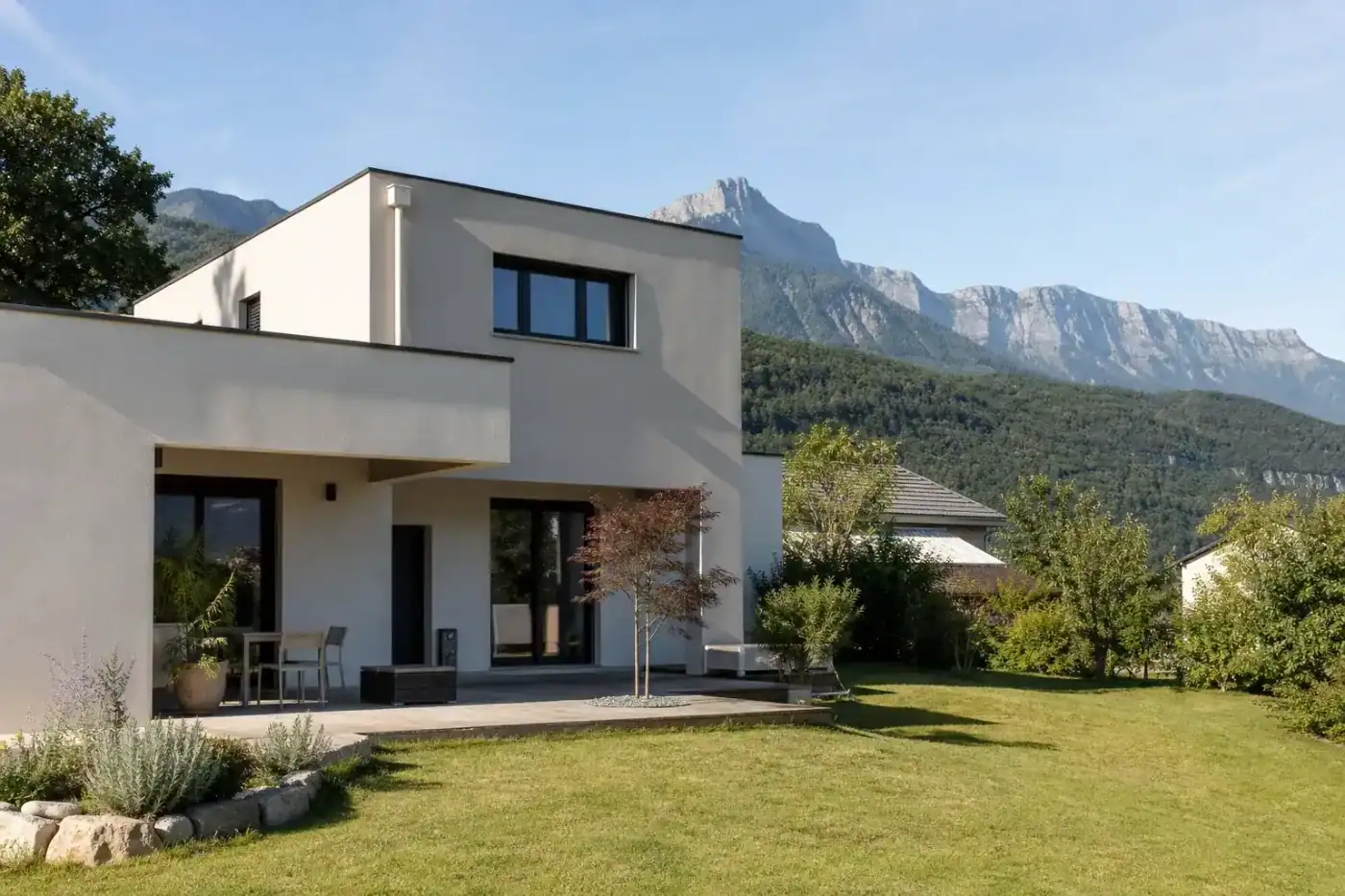 maison individuelle familiale avec jardin engazonné, entrée de vallée montagneuse en arrière-plan, matin ensoleillé, aucune personne visible