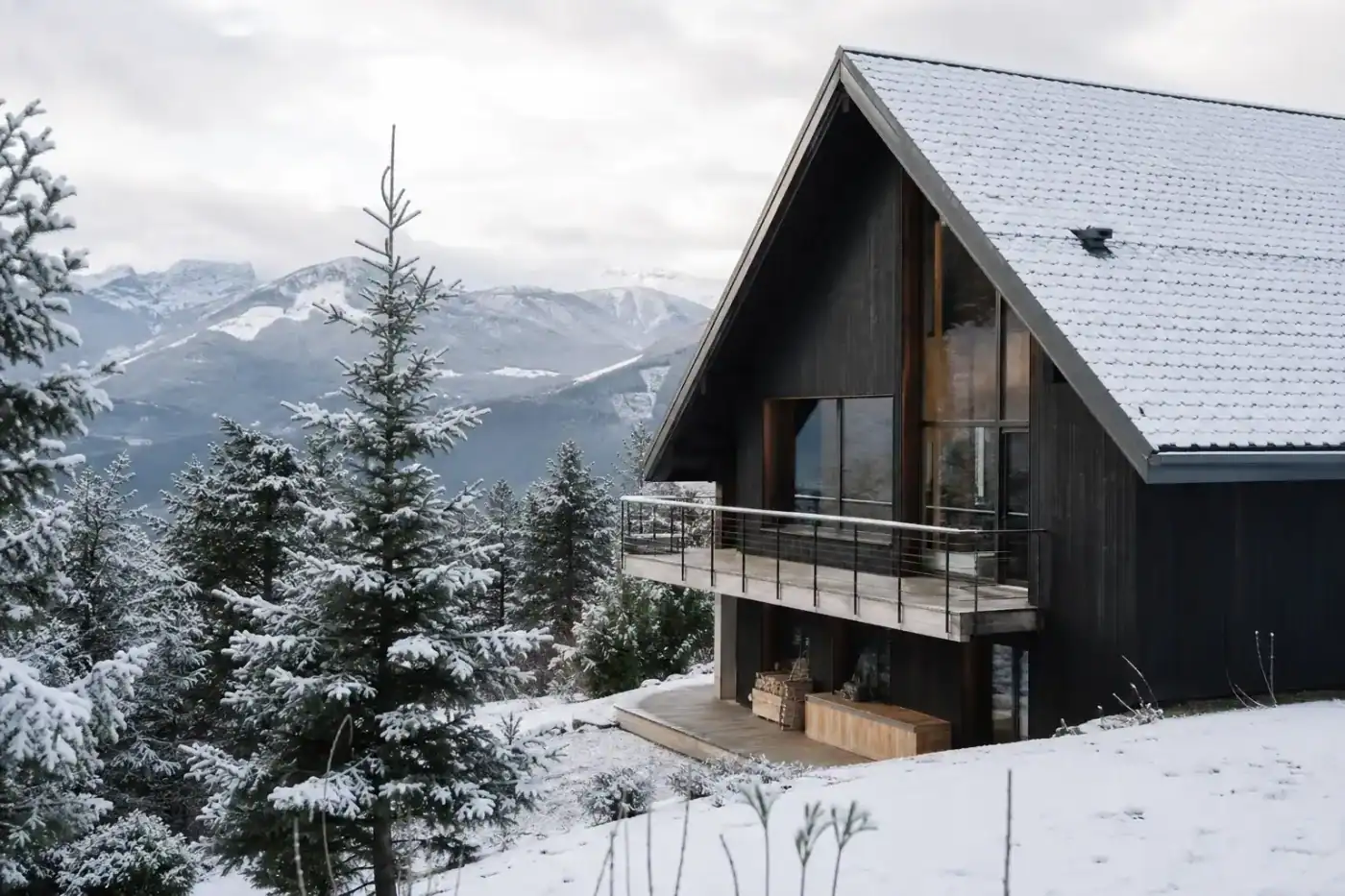 chalet de montagne contemporain, bardage bois foncé, toit à forte pente couvert de neige légère, sapins alentour, lumière d'hiver, aucune personne visible