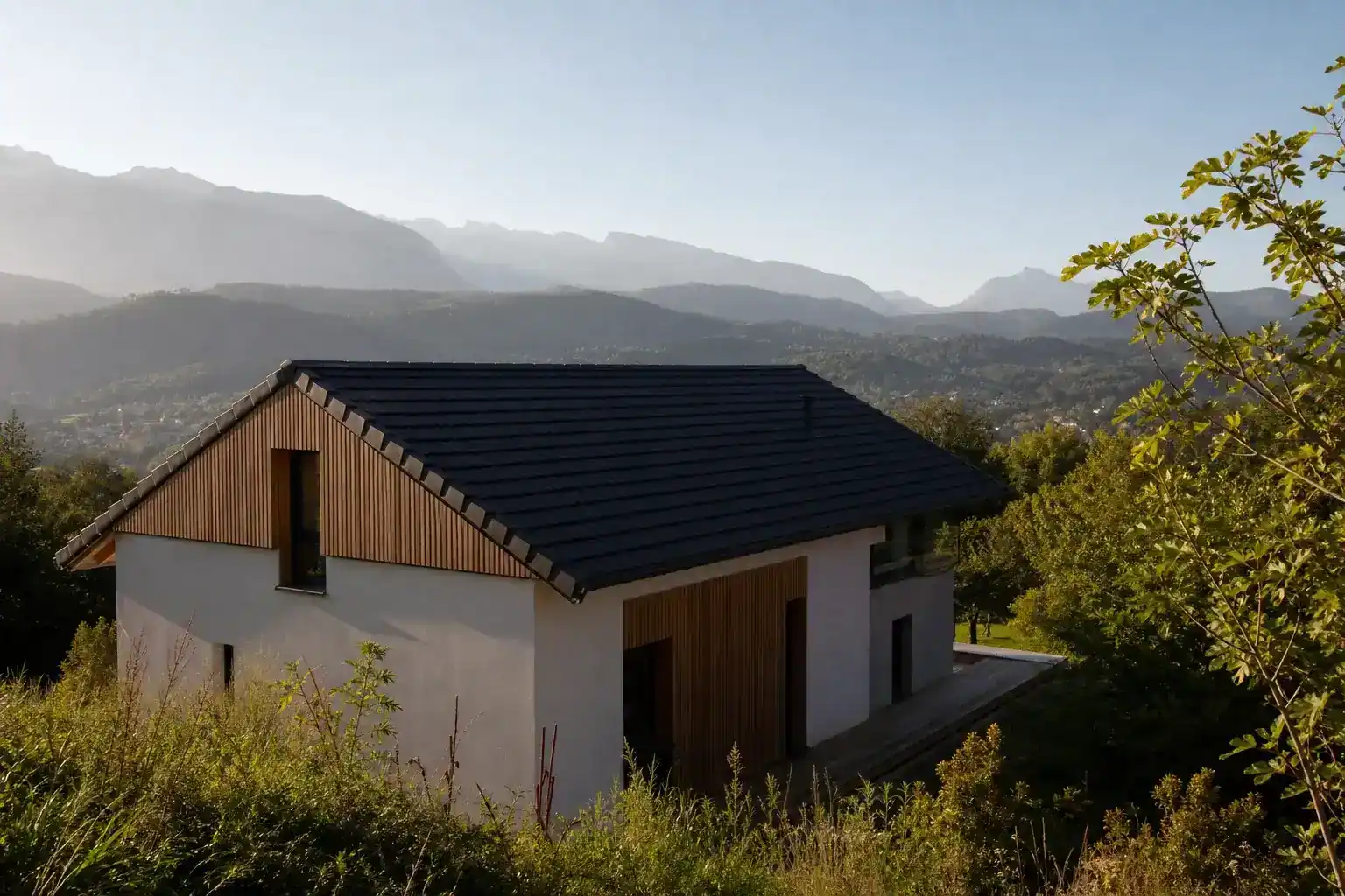maison individuelle récente à toit à deux pans, bardage bois partiel, fond de vallée avec relief montagneux, lumière de matin, aucune personne visible
