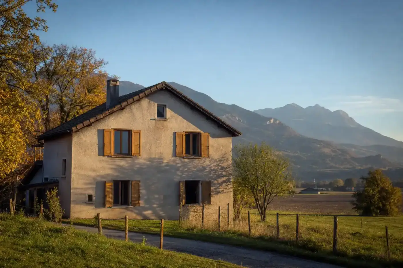 maison rurale traditionnelle entourée de terres agricoles, façade enduite claire, volets bois, lumière de fin de journée, aucune personne visible